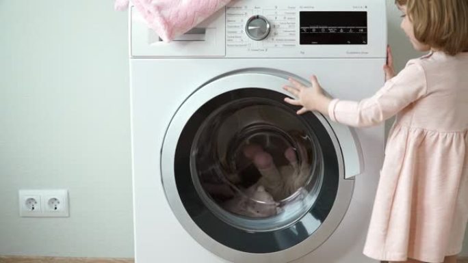 小微笑可爱的3岁女孩的肖像放入洗衣机玩具洗涤，关闭舱门并打开家用电器