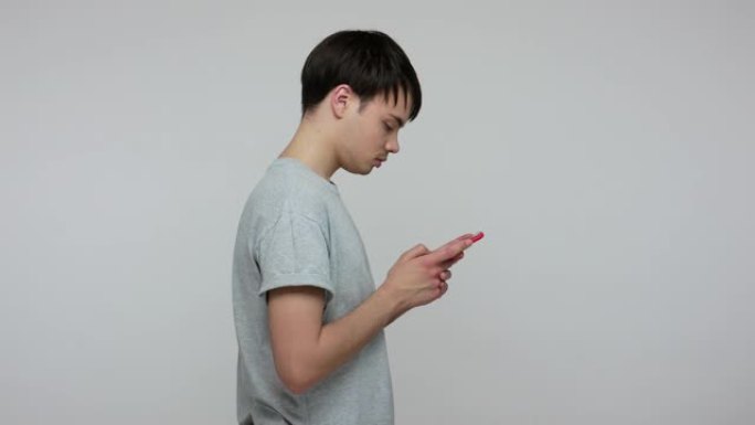 移动通信。穿着t恤的年轻黑发男人在手机上打字信息，在社交网络上聊天的侧视图