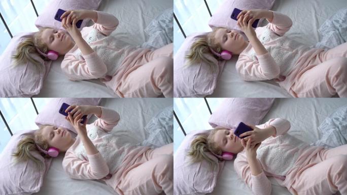 Z世代的现代生活。穿着睡衣和耳机的少女在床上的房间里听智能手机的音乐。