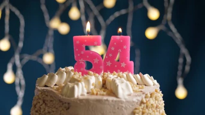 蓝色背景上有54号粉色蜡烛的生日蛋糕。蜡烛吹灭了。慢动作和特写视图