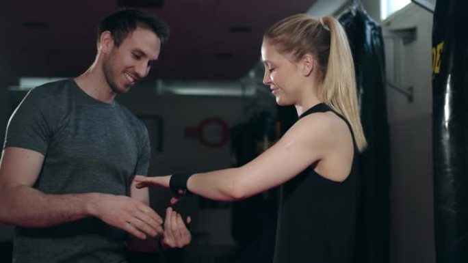 拳击教练帮助他的客户，一个年轻的女人包裹她的手