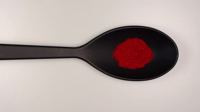 俯视图: 红辣椒粉在白色桌子上装满黑色塑料勺子-停止运动