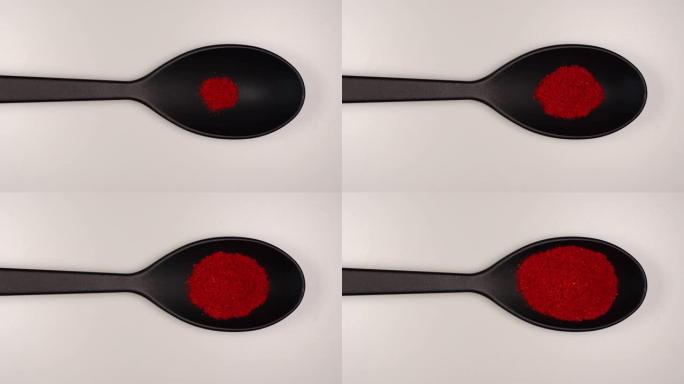 俯视图: 红辣椒粉在白色桌子上装满黑色塑料勺子-停止运动