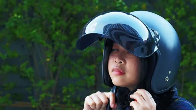 一名年轻女子系紧或戴摩托车头盔，模糊福建茶树Carmona retusa绿色背景-零事故概念