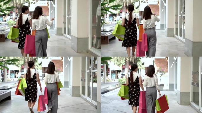 购物中心两个美女的肖像看着商店的橱窗和微笑