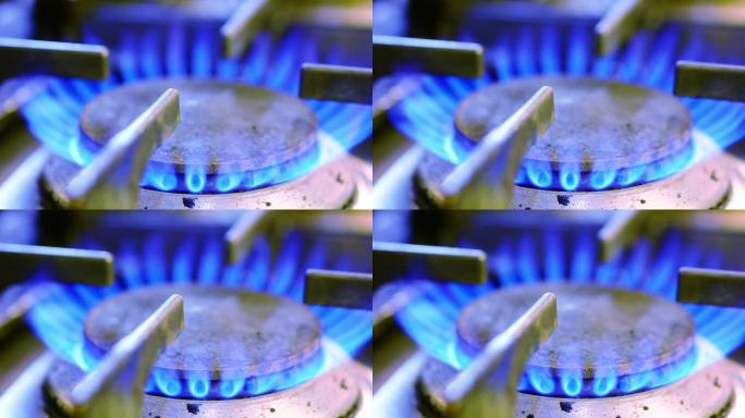 厨房炉灶上的燃气燃烧器，带有燃烧的蓝色火焰。