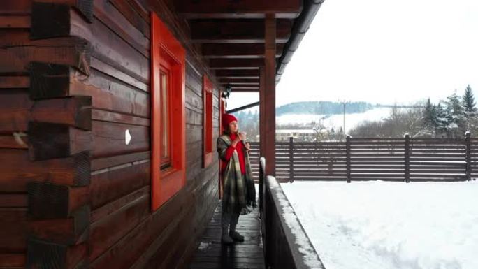 4k女人冬天穿着红色豆豆在木制避暑别墅的露台上喝茶