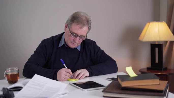 白人老人写笔记，贴在桌子上的物体上。眼镜中的成熟退休人员与疾病和衰老作斗争。生活方式，问题，阿尔茨海