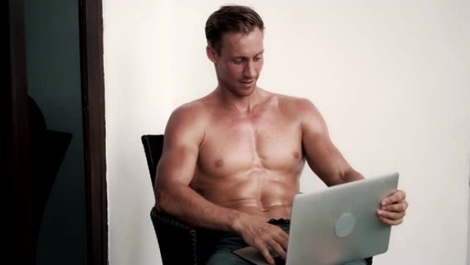 赤裸上身的男人与性感的身体坐在椅子上与笔记本电脑，谈论网络摄像头，笑
