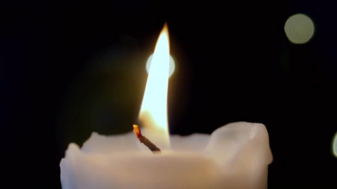在黑暗背景中燃烧的单个白色蜡烛的特写镜头。4K