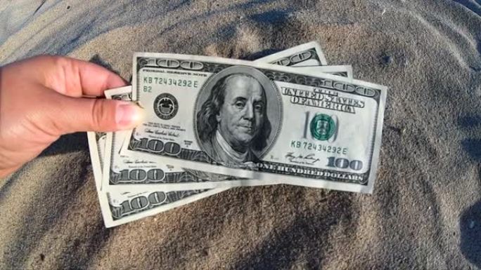 女孩拿着一张300美元的钞票，背景是海洋的沙子