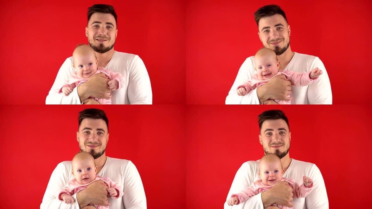 年轻的父亲带着一个婴儿，亲吻一个婴儿，他微笑着。家庭概念，爸爸概念。爸爸是个家庭主妇。在红色背景上隔