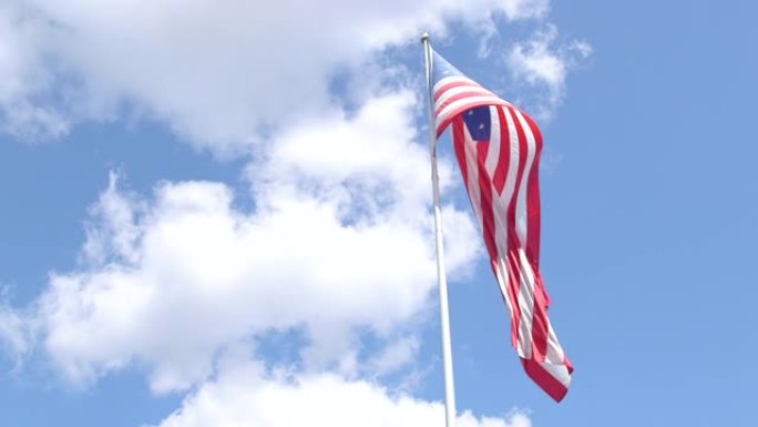 巨大的美国国旗在明亮的蓝色多云天空下飘扬