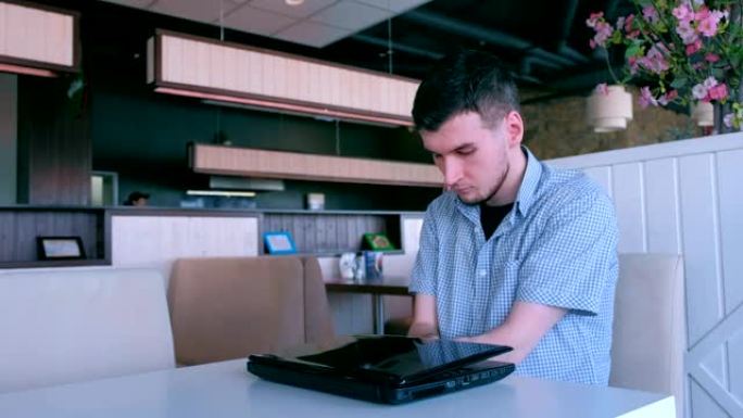 一位双手截肢的年轻残疾人在咖啡馆用笔记本电脑工作。