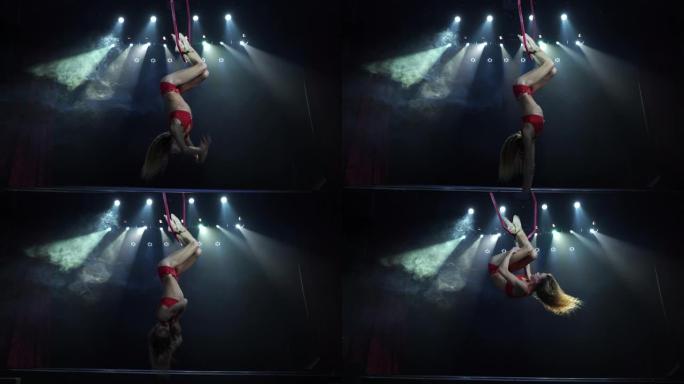 舞台上苗条性感的女性空中杂技演员，背景上有聚光灯的空中箍