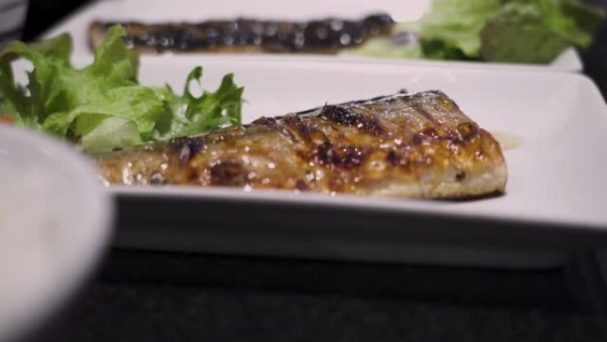 4k特写烤鱼saba在白盘，日本料理，午餐时间，亚洲料理，欧米茄3，海鱼餐，白色荧光灯，黑色桌子，绿