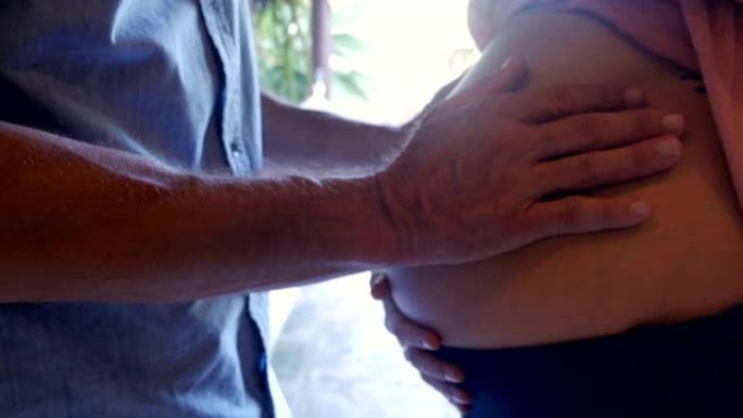 一个男人用双手抚摸女人怀孕的肚子的特写