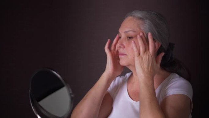 年长的女人在镜子里看到并在脸上涂上奶油