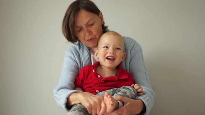 幸福的祖母和她的小孙子的近照。女人把孩子抱在怀里，挠他的脚后跟，婴儿欢笑。家庭周末快乐