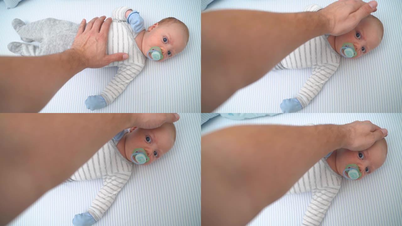 父亲男性的手抚摸着躺在婴儿床里吮吸奶嘴母猪运动的男婴