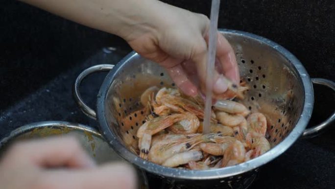 水槽中洗虾的过程。女人在家庭厨房洗虾。家庭烹饪。厨师煮虾。健康食品概念。女性烹饪海鲜