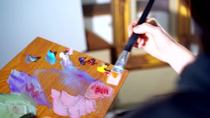 调色板在女艺术家的手中，才华横溢的画家拿着专业的画笔，在木板上慢慢混合不同的油画。艺术家混合红色和白