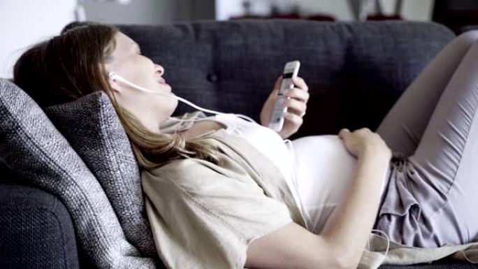 微笑的孕妇躺在沙发上有视频通话