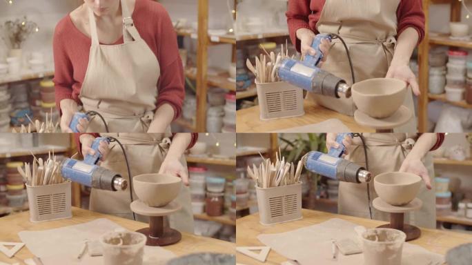工作室用热风枪烘干陶器碗的女工匠
