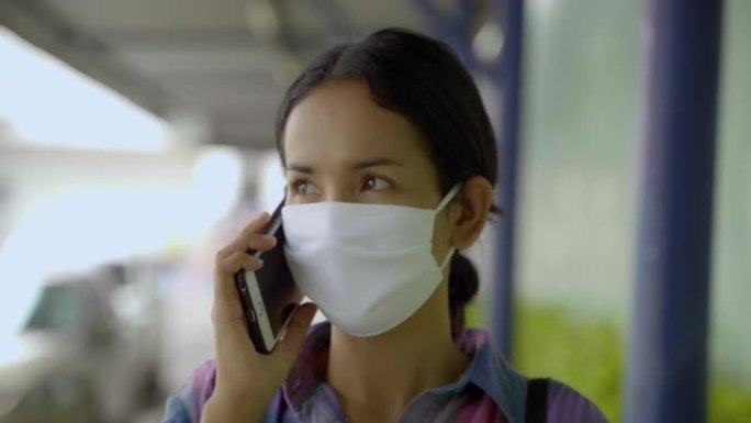 年轻的亚洲女人玩智能手机与面罩保护免受不良污染和病毒。