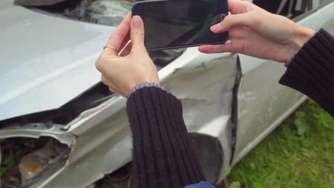 一辆破车撞车后，女人在智能手机上拍照
