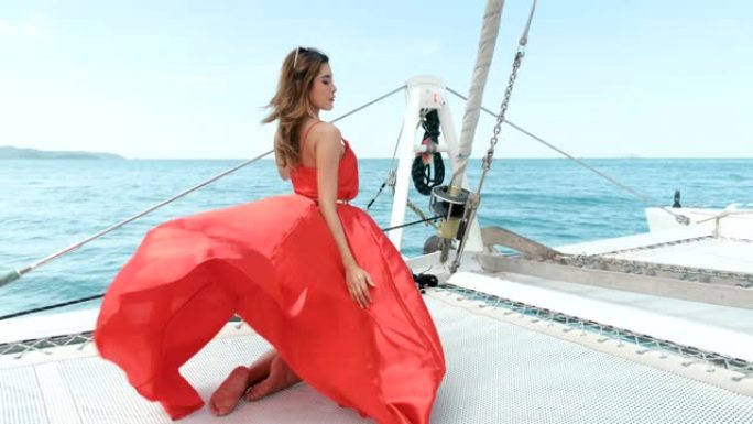 穿着比基尼的亚洲红色连衣裙女孩站在游艇的船头，在阳光照射下看起来放松和性感的姿势。