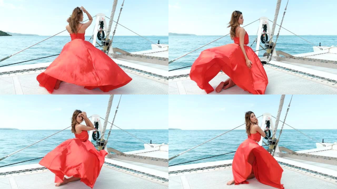 穿着比基尼的亚洲红色连衣裙女孩站在游艇的船头，在阳光照射下看起来放松和性感的姿势。