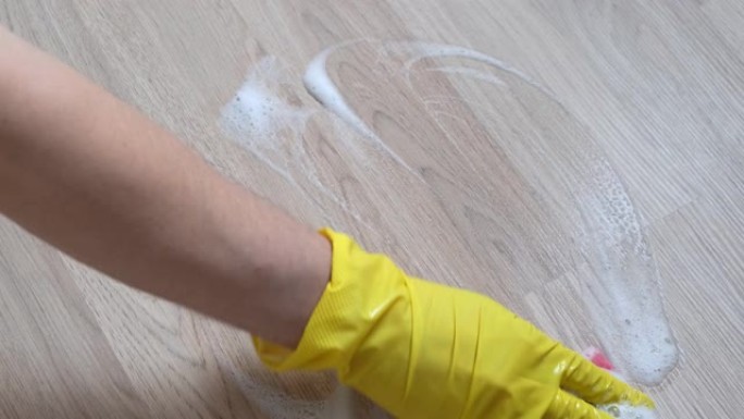一只戴着黄色手套的女性手擦拭木质表面。特写。