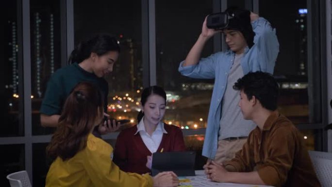 亚洲ux开发人员和ui设计师在夜间与城市之光的现代办公室中使用移动应用程序原型设计检查虚拟现实眼镜。
