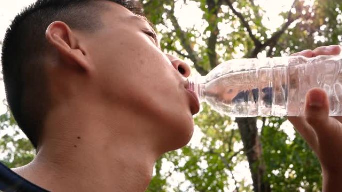 亚洲十几岁的男孩在公园慢跑后从瓶子里喝水。