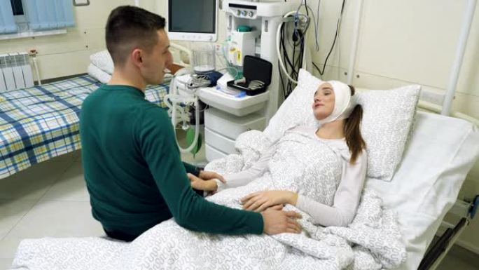睡在病床上的女病人。年轻的丈夫去诊所看望妻子。一个男人轻轻地亲吻一个迷人的女人。4K