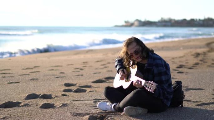 度假时坐在沙滩上玩经典吉他的帅哥