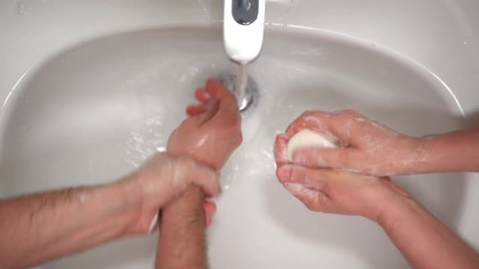 两个人在浴室或厕所的温水下用消毒剂肥皂洗手的俯视图。日常卫生，严格说明防止病毒或微生物在人群中膨胀。