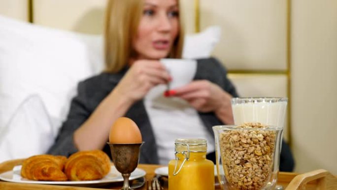 年轻相当成功的女商人在豪华酒店房间吃早餐。光线酒店公寓里的女孩早上在小桌子托盘上享受咖啡，4k拍摄