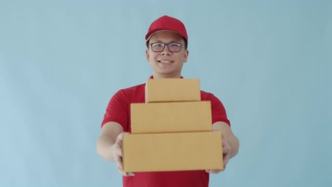 亚洲快乐送货员携带纸质包裹箱，孤立在蓝色背景上，面带微笑。邮政递送服务的概念。