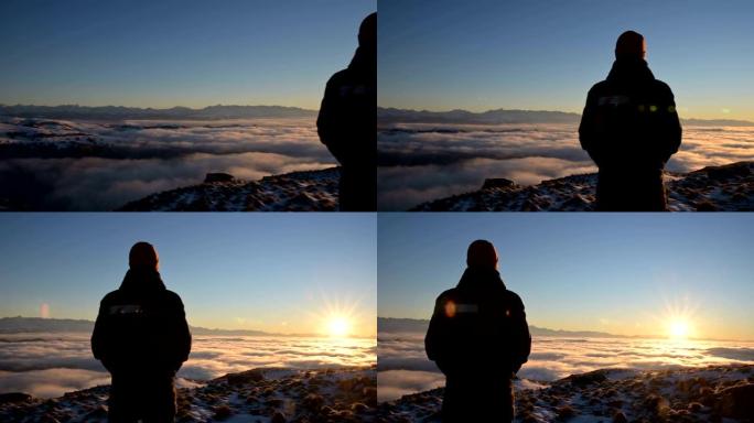 从后面看。一个孤独的站立在高山上的人看着夕阳和日落的地平线，那里充满了云层。旅游旅行与男性孤独的概念
