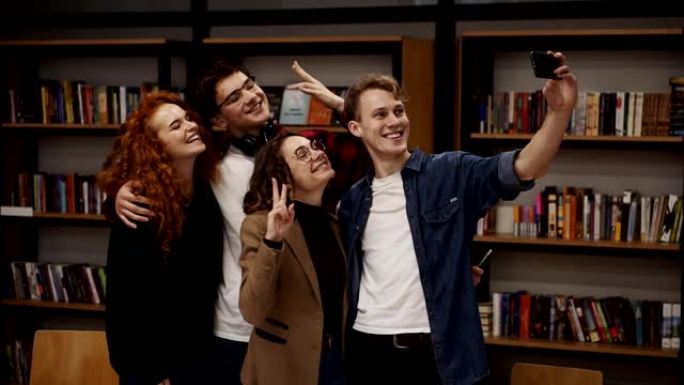 欧洲学生，四人一组在学院或大学图书馆自拍。四人一组站在书架前，开心地微笑着，打手势，表现出和平的姿态