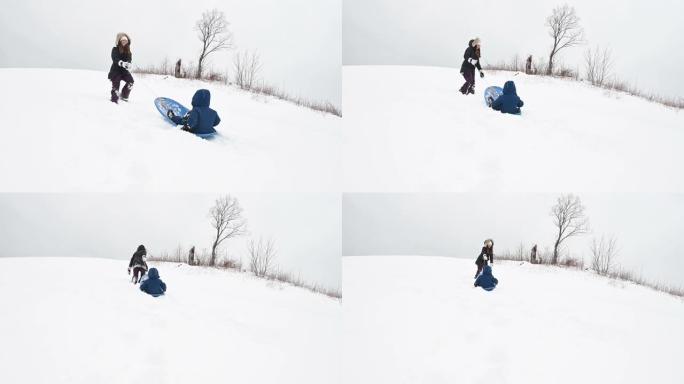 儿子和母亲在雪山冬季运动雪橇上玩耍
