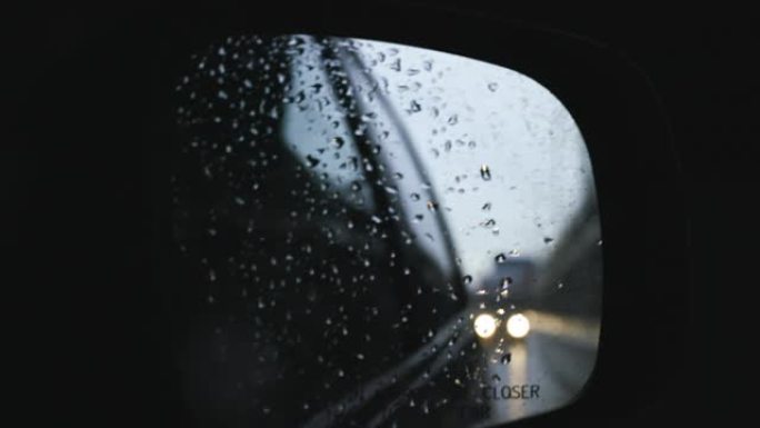 当车辆在高速公路上行驶时，汽车侧镜的慢动作镜头被雨滴覆盖。