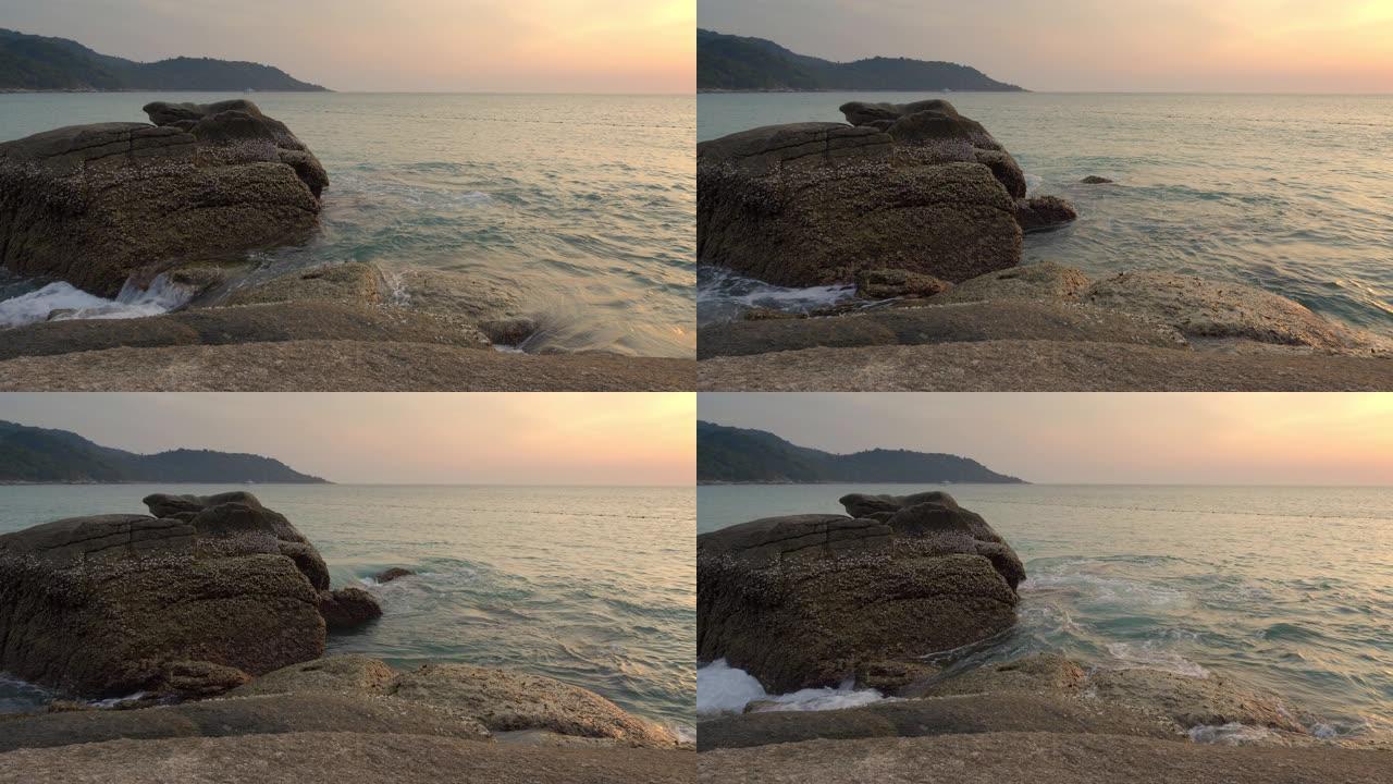 日落时热带海滩附近覆盖着贝壳的大黑石