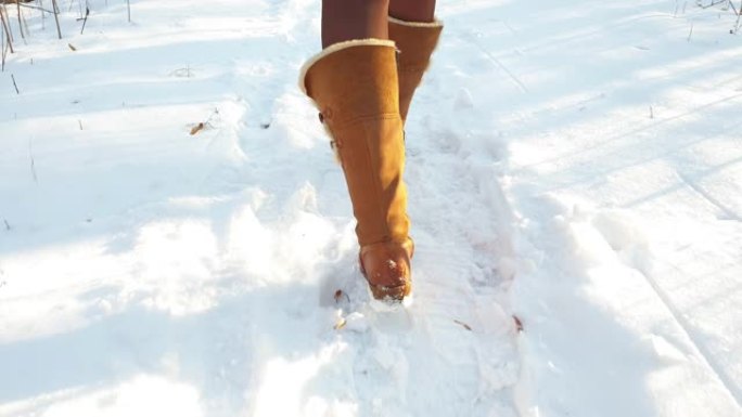 腿部女人冬季棕色皮靴和连裤袜在冬季公园的雪地上行走。暖靴特写外底
