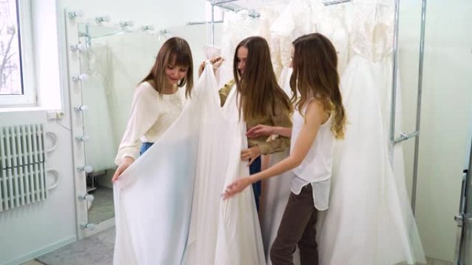 兴奋的新娘和伴娘在婚礼沙龙试穿时尚的白色礼服