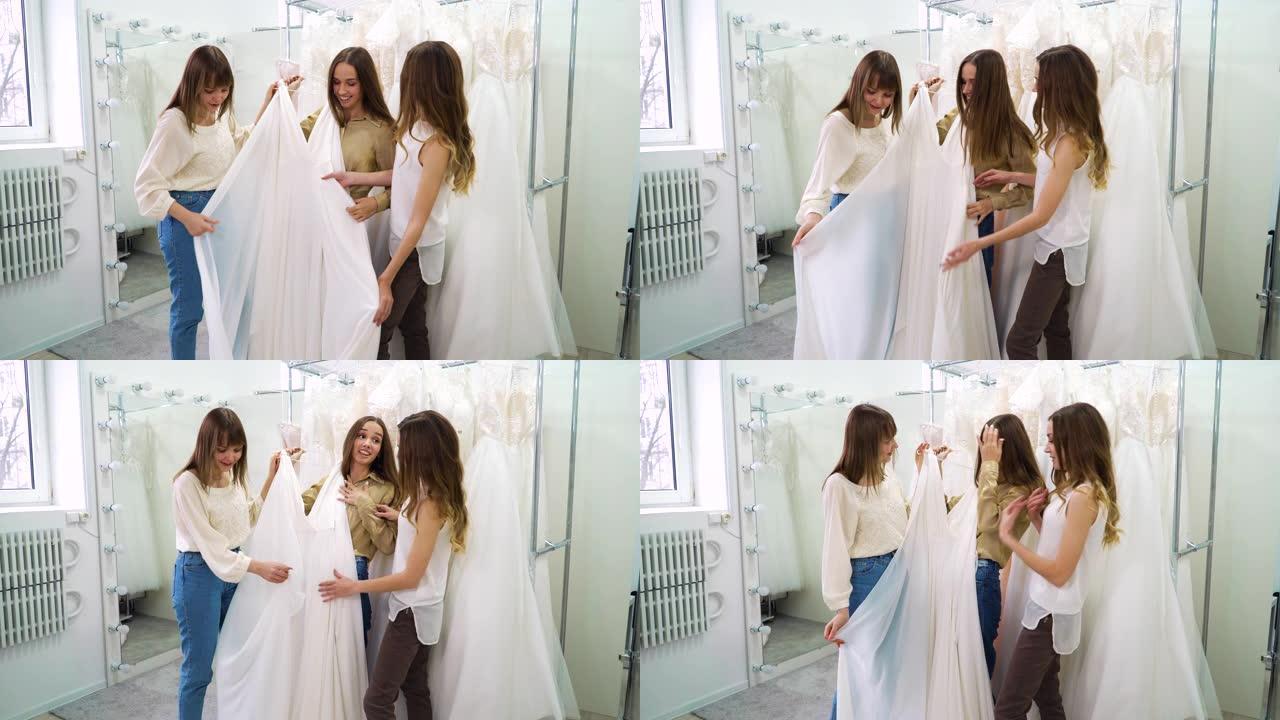 兴奋的新娘和伴娘在婚礼沙龙试穿时尚的白色礼服