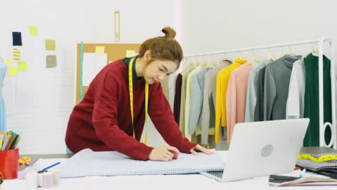 亚洲女性时装设计师在亚洲小型企业家庭工作室的办公桌上使用面料