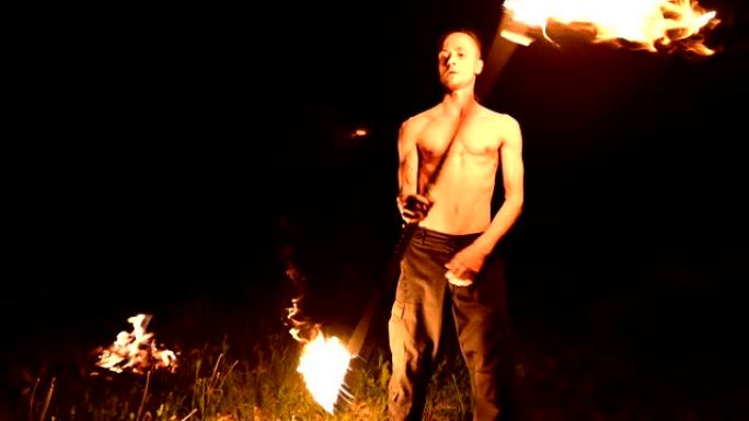 低调。长发，裸露躯干的年轻男性在黑色夜晚视频慢动作中在户外旋转燃烧的火炬。现代法克尔 (fakir)
